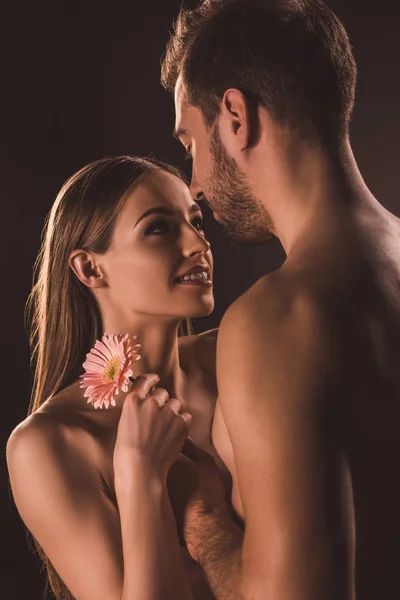 Schöne Liebende, die einander anschauen und Gerbera-Blüten in der Hand halten, isoliert auf braun — Stockfoto