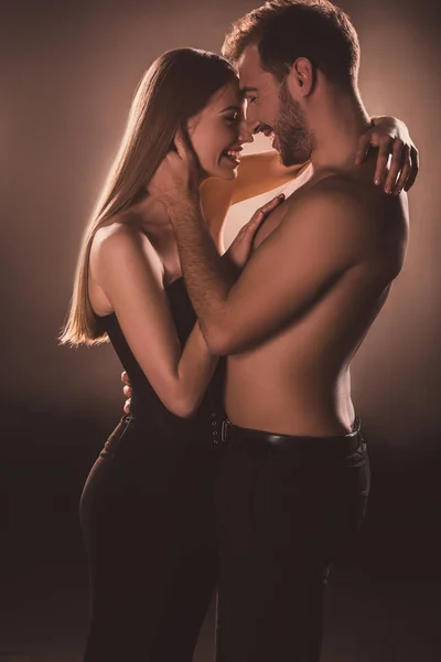 Pareja sensual riendo y abrazándose juntos, en marrón con luz de fondo - foto de stock