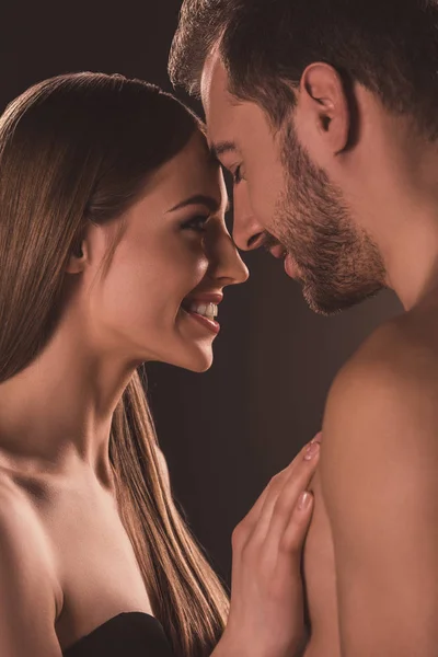 Sonriente pareja desnuda abrazándose y mirándose, en marrón - foto de stock