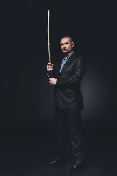 Homme sérieux en costume avec katana japonais épée sur noir — Photo de stock