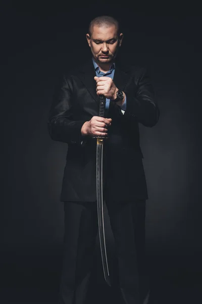 Hombre de traje con espada katana japonesa sobre negro - foto de stock