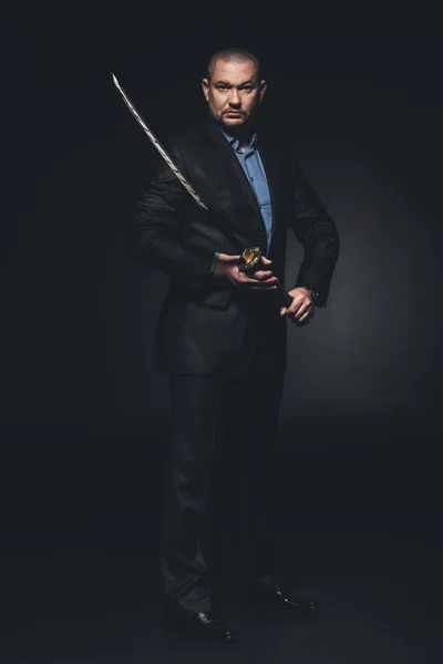 Älterer Mann im Anzug mit japanischem Katana-Schwert auf Schwarz — Stockfoto