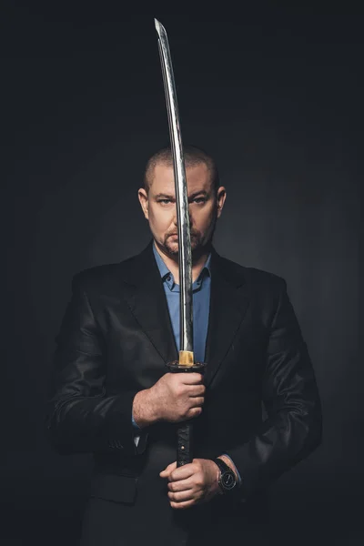 Mature man in suit holding japanese katana sword in front of his face isolated on black — Stock Photo