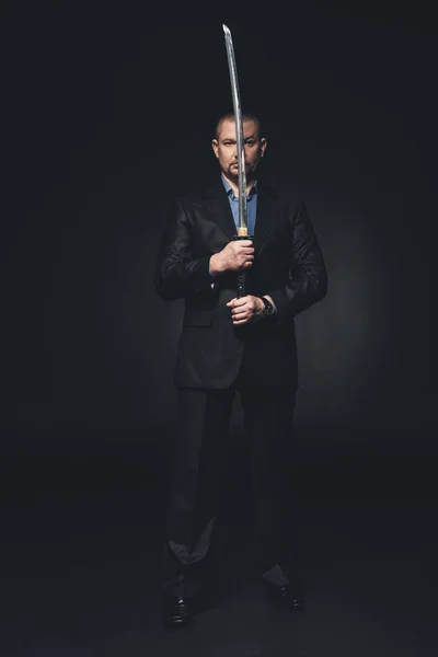 Man in suit holding japanese katana sword in front of his face on black — Stock Photo