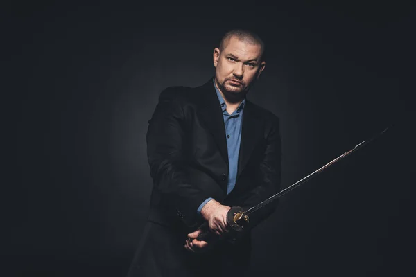 Serious man in suit with katana on black — Stock Photo