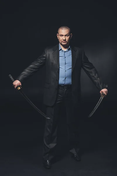 Handsome serious man in suit with dual katana swords on black — Stock Photo