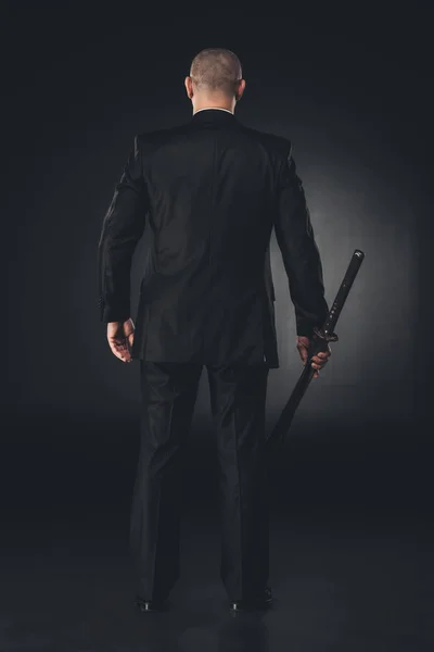 Rear view of man in suit with katana sword on black — Stock Photo