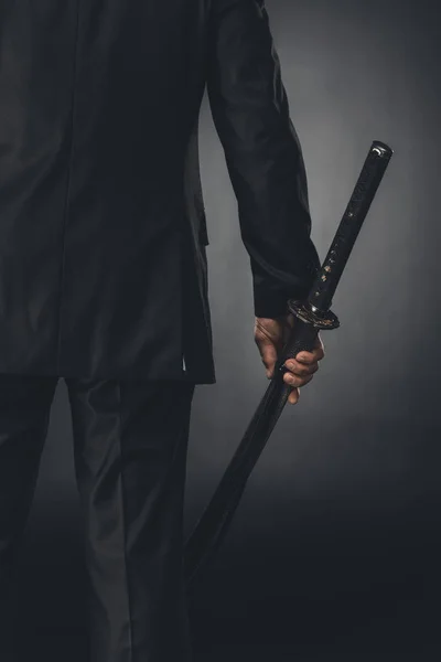Обрезанный снимок человека в деловом костюме с мечом катаны на черном — стоковое фото