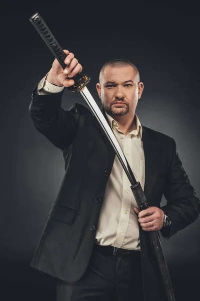 Homme en costume prise de son épée katana sur noir — Photo de stock