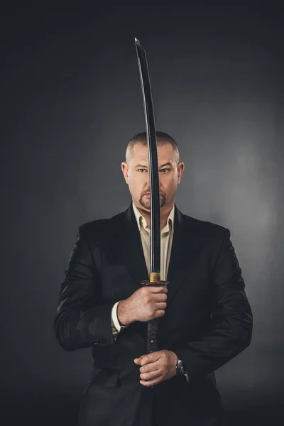 Man in suit holding katana sword in front of his face on black — Stock Photo