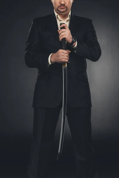 Cropped shot of yakuza member in suit holding katana sword on black — Stock Photo