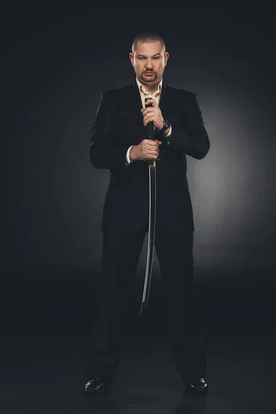 Serious yakuza member in suit holding katana sword on black — Stock Photo