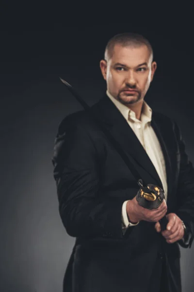 Guapo hombre maduro en traje con espada katana en negro — Stock Photo