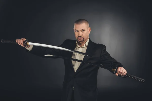 Серьезный человек в костюме с двумя катаными мечами на черном — стоковое фото