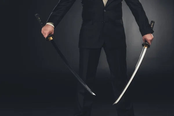 Cropped shot of man in suit with dual katana swords on dark background — Stock Photo