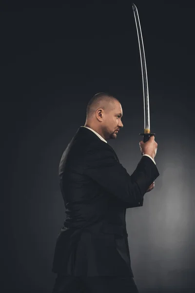 Боковой вид зрелого члена якудза в костюме с мечом катаны на черном — стоковое фото