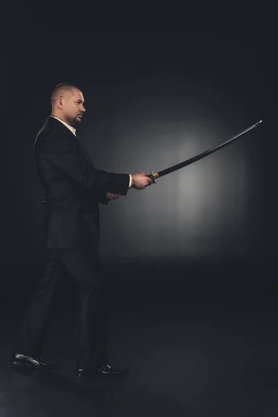 Side view of mature man in suit with katana sword on dark background — Stock Photo