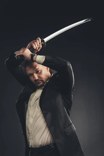 Serious mature man in suit with katana sword isolated on black — Stock Photo