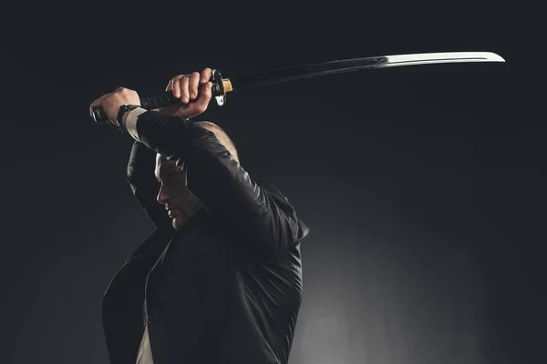 Вид збоку чоловіка в костюмі, який вдарив катаною мечем ізольовано на чорному — стокове фото