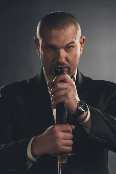 Close-up portrait of adult man in suit with katana sword on black — Stock Photo