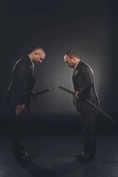 Side view of yakuza members in suits bowing to each other isolated on black — Stock Photo