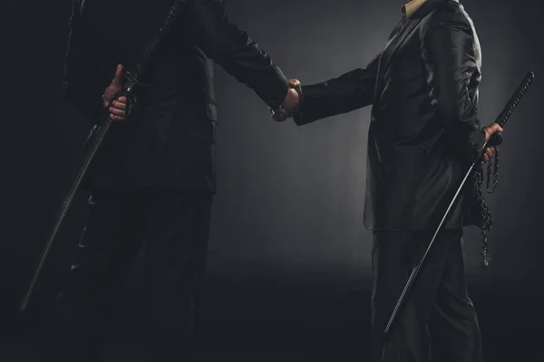 Abgeschnittene Aufnahme von Yakuza-Mitgliedern beim Händeschütteln mit Katanas hinter dem Rücken isoliert auf schwarz — Stockfoto