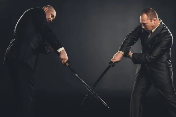 Homens de negócios lutando com espadas de katana isolados em preto — Fotografia de Stock