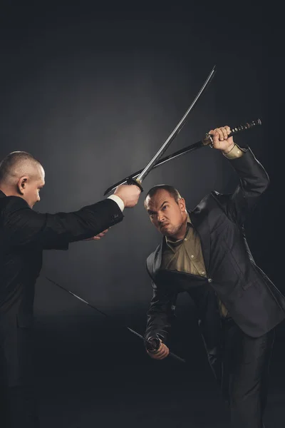 Modern samurai in suits fighting with swords on black — Stock Photo