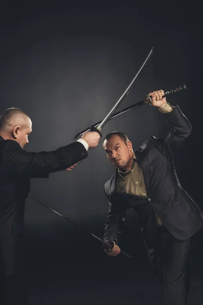 Samurai moderno en trajes que luchan con espadas sobre negro - foto de stock