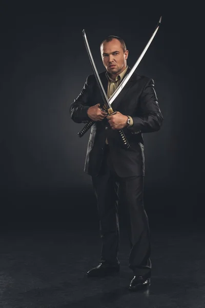 Handsome man in suit with dual katana swords on black — Stock Photo