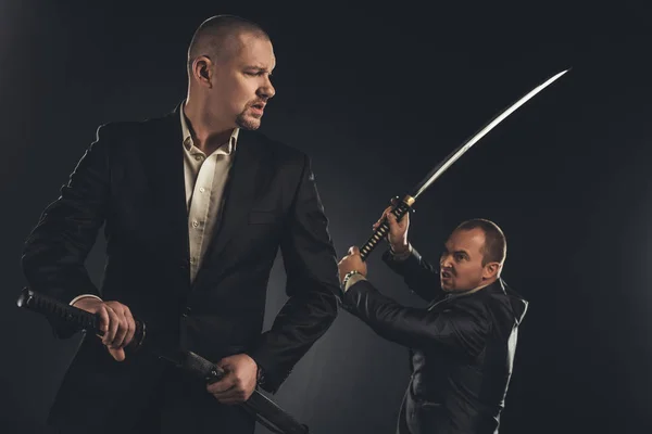 Modern samurai in suits with katana swords isolated on black — Stock Photo