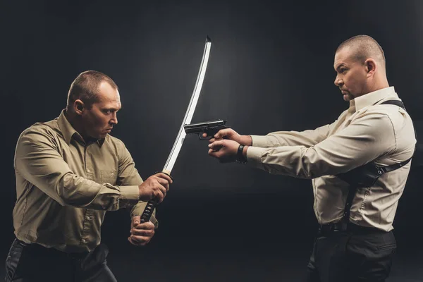 Side view of men fighting with gun and katana sword on black — Stock Photo