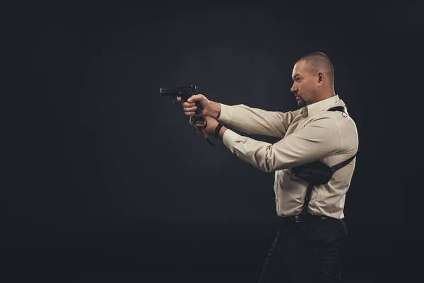 Side view of killer holding gun isolated on black — Stock Photo