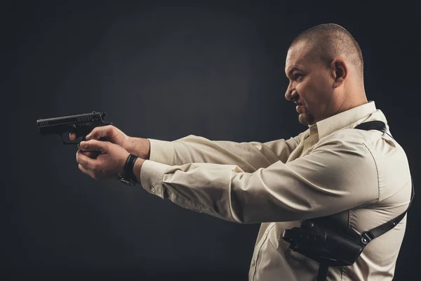 Side view of man in shirt holding gun isolated on black — Stock Photo