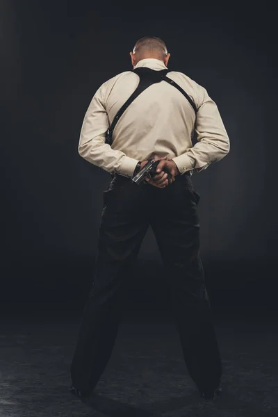 Back view of killer in shirt holding gun behind back — Stock Photo