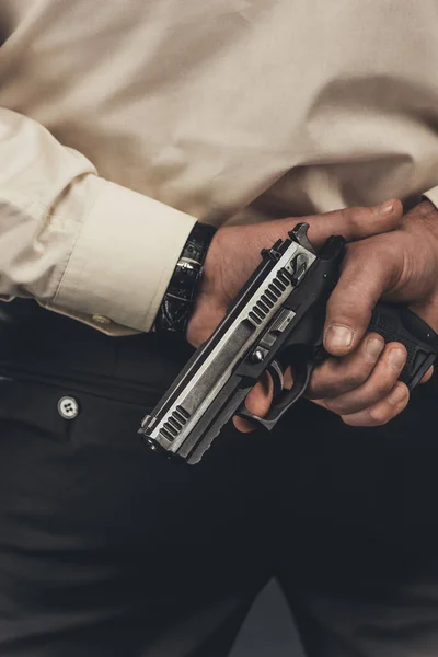 Cropped shot of man in shirt holding gun behind back — Stock Photo