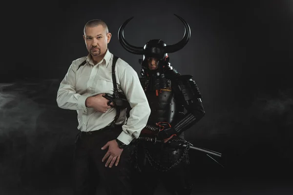 Hombre con arma y samurai blindado detrás de él en negro - foto de stock