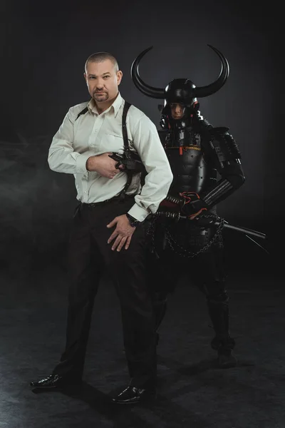 Homem com arma e samurai atrás dele em preto — Fotografia de Stock