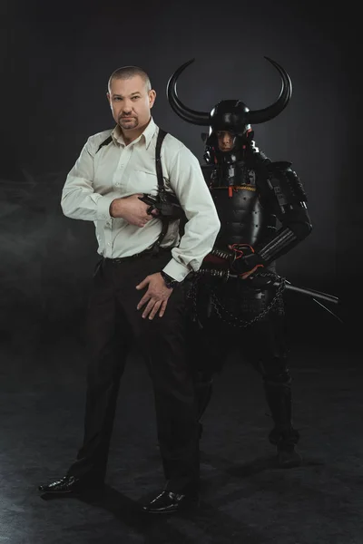 Man with gun and samurai behind him on black — Stock Photo