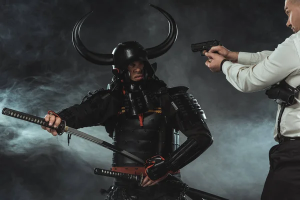 Hombre moderno apuntando a samurai con un arma mientras saca su espada - foto de stock