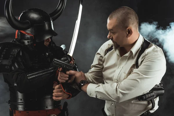 Armored samurai fighting with modern man in shirt who holding gun — Stock Photo