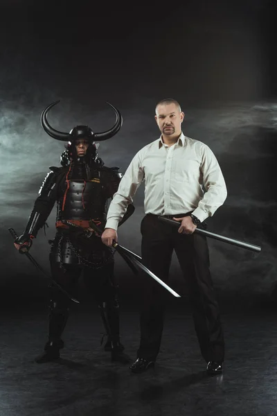 Uomo moderno e samurai con spade katana su nero — Foto stock