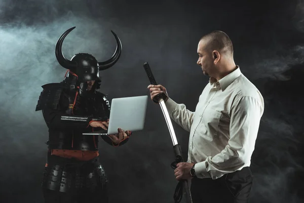 Man with katana standing in fornt of samurai while he using laptop — Stock Photo