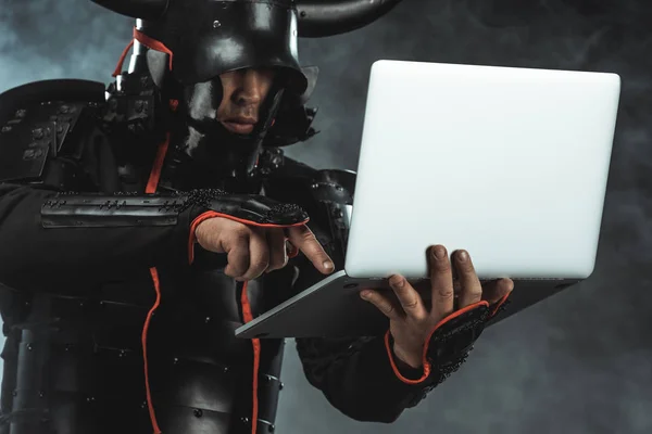 Close-up shot of samurai using laptop on dark background with smoke — Stock Photo