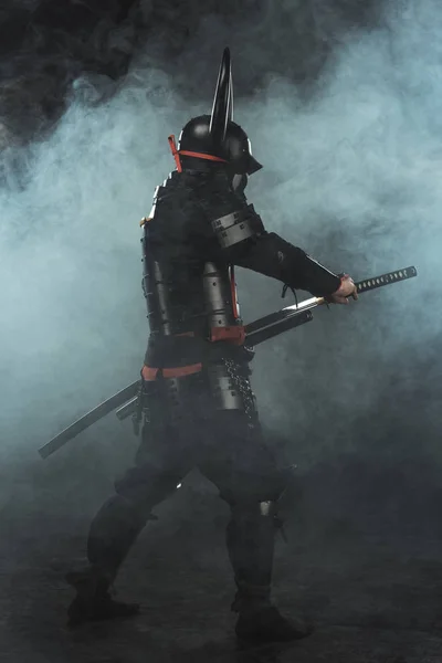 Vista lateral do samurai tirando sua katana no fundo escuro com fumaça — Fotografia de Stock