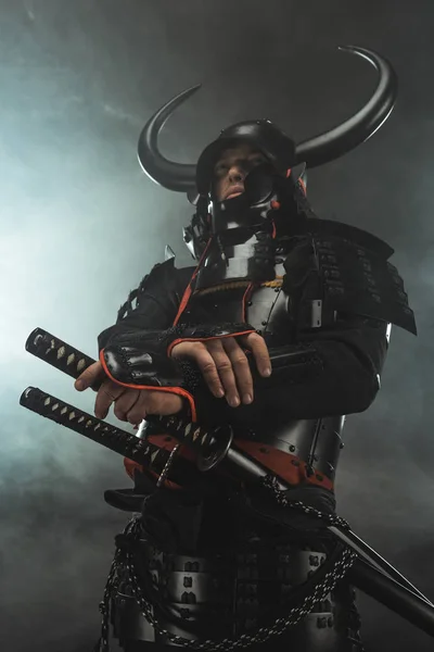 Bottom view of samurai in traditional armor with swords on dark background with smoke — Stock Photo