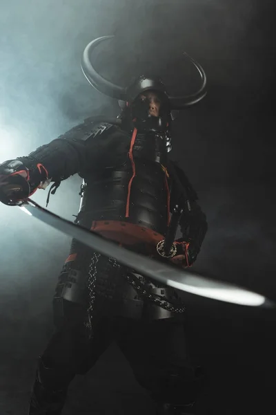 Bottom view of samurai in traditional armor with sword on dark background with smoke — Stock Photo