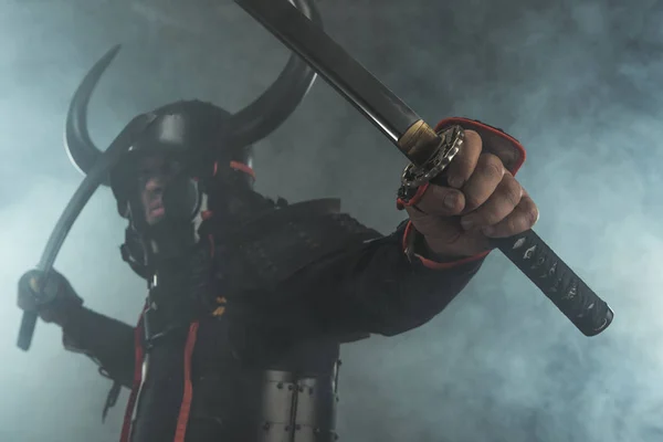 Primer plano de samurai en armadura con espadas duales de katana sobre fondo oscuro con humo - foto de stock