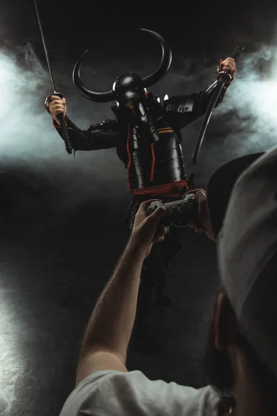 Человек, управляющий самурайским характером с геймпадом на черном — стоковое фото