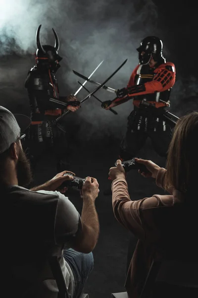 Back view of man and woman playing samurai fighting in real life with gamepads on black — Stock Photo